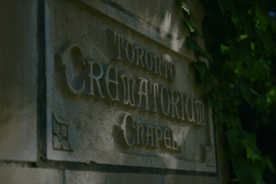 Close‑up of carved stone signage reading “Toronto Crematorium Chapel,” partially framed by green ivy growing along the edge of the building.