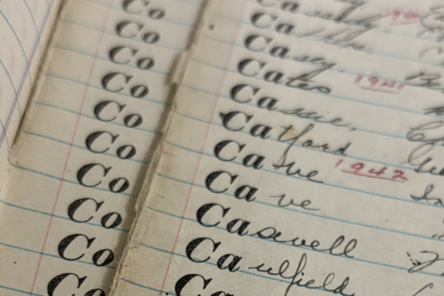 Close‑up of an open handwritten ledger showing neat cursive entries written in black ink on lined paper, with repeated surnames listed in columns across facing pages.