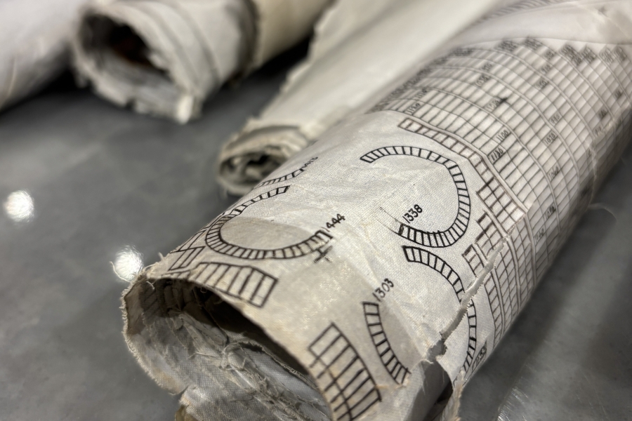 Rolled architectural or technical drawings resting on a table, showing printed measurement markings and curved line diagrams on aged, slightly torn paper.