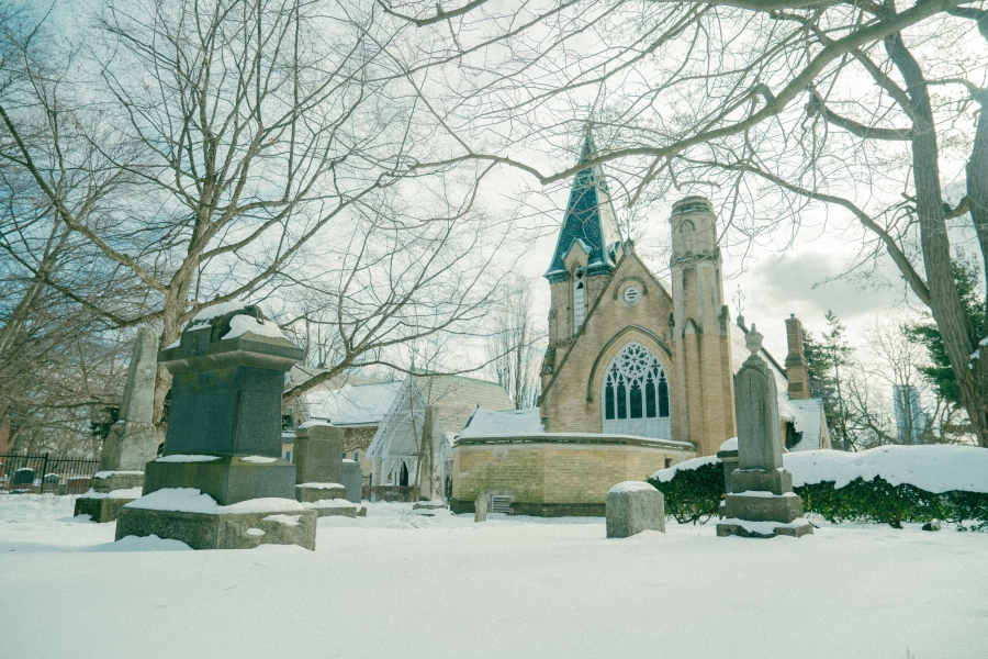 Winter view of the Toronto Crematorium and Necropolis Chapel, showing the Gothic chapel surrounded by snow‑covered ground, headstones, and leafless trees within a historic cemetery.