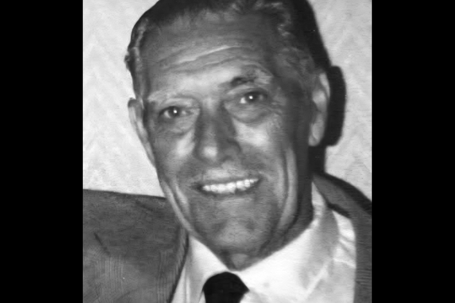 Black and white photo of Lloyd Shaddock. He is smiling and wearing a suit jacket, white shirt and black tie. His hair is well-kempt and short.