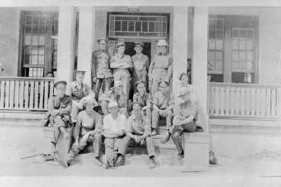 Black‑and‑white photograph of soldiers seated around tables inside a military convalescent hospital common room, with a nurse standing nearby and a piano against the wall, light streaming in through tall windows.