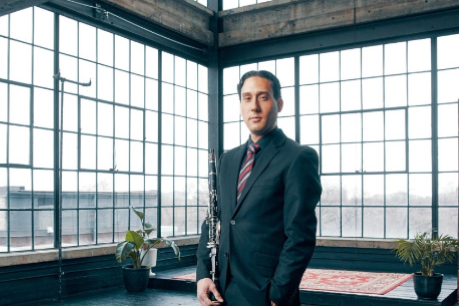 Person in a suit standing in a large industrial-style room with tall windows, holding a clarinet. Provide your feedback on BizChat