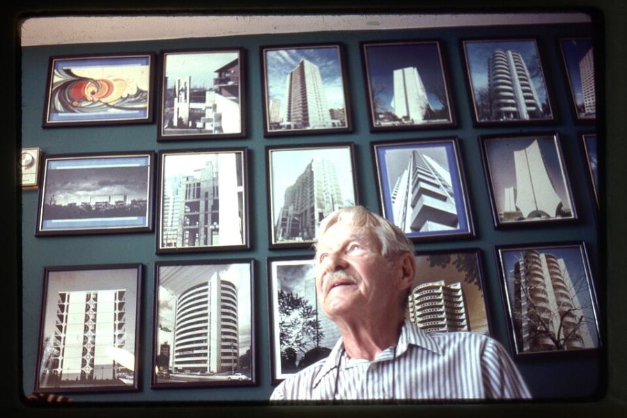 man standing behind a wall with framed photos of buildings