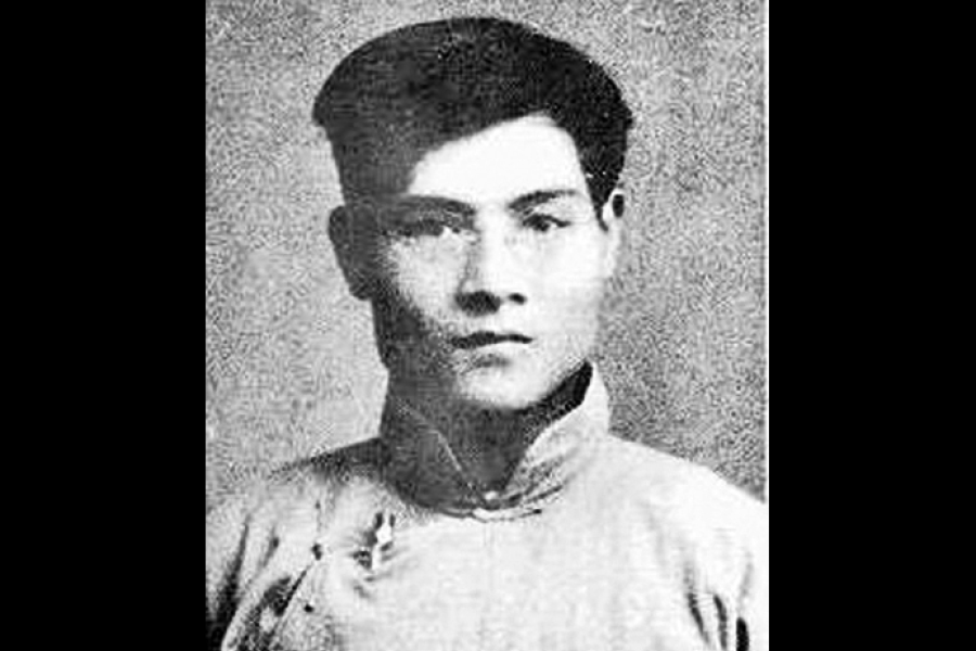 Black‑and‑white portrait of a person wearing a cap and a simple, long‑sleeved shirt, photographed from the chest up against a plain textured background.