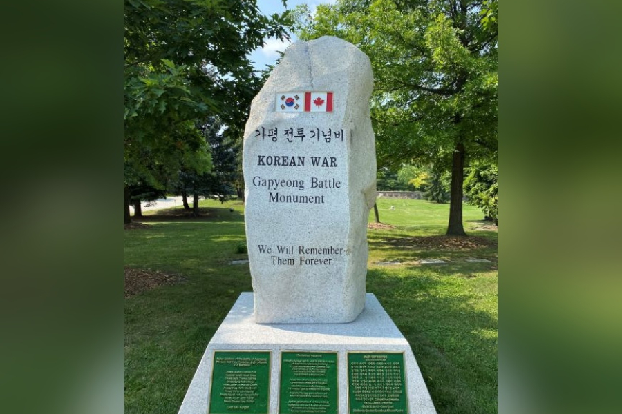 Taller stone memorial monument set in a green park, inscribed with the words “Korean War Gapyeong Battle Monument” and “We Will Remember Them Forever,” featuring the South Korean and Canadian flags at the top, with engraved bronze plaques mounted on the base and trees surrounding the site.