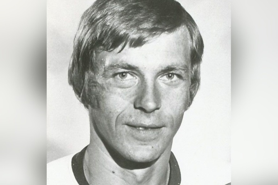 Black‑and‑white portrait of Nick Harbaruk shown from the shoulders up, with medium‑length hair parted to the side, wearing a collared athletic‑style shirt, photographed against a plain light background.