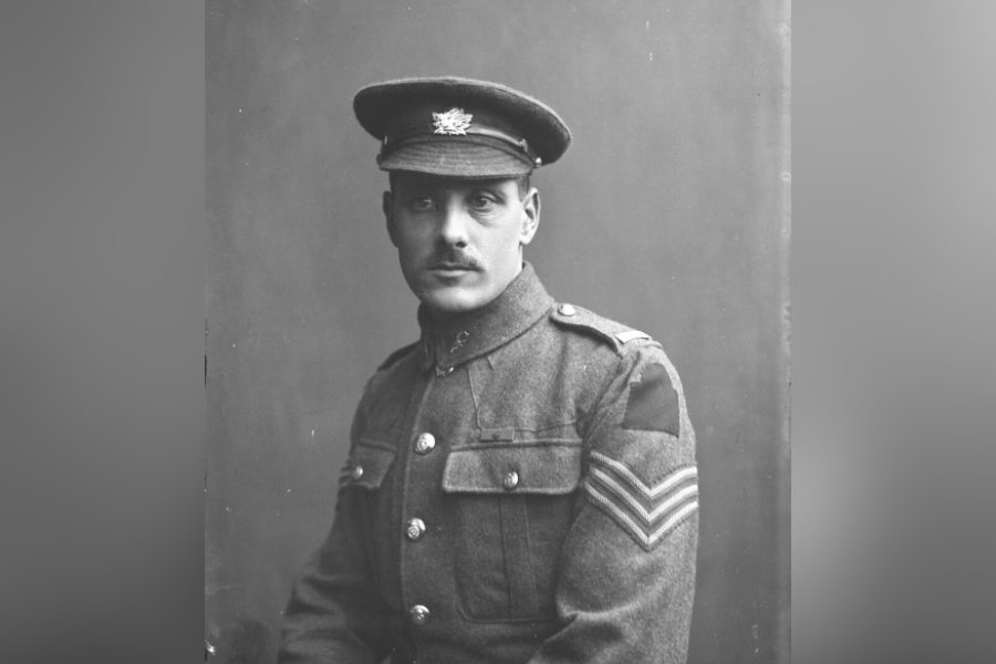  Black-and-white studio portrait of Private Walter Leigh Rayfield, V.C., seated in uniform wearing a service cap and a buttoned military tunic with chevrons on the sleeve, posed against a plain backdrop.