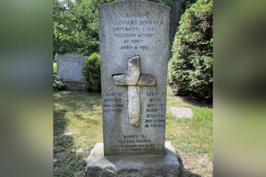 Stone grave marker for Captain Stewart Boulter featuring a carved cross set into the centre of the monument, with engraved text commemorating his military service and death in action during the First World War, standing on a stone base in a grassy cemetery surrounded by trees.