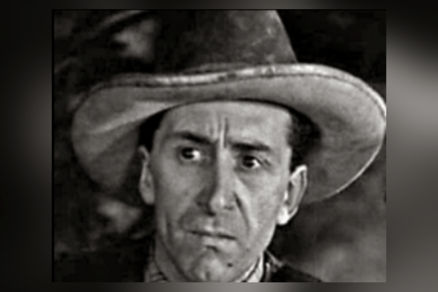 Black‑and‑white portrait of Eric Clavering wearing a wide‑brimmed hat and dark coat, shown from the shoulders up against a softly out‑of‑focus background.