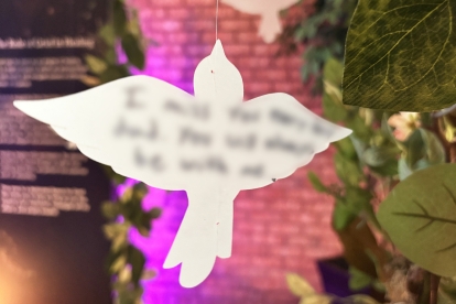 White bird-shaped ornament hanging in front of greenery with soft colored lighting