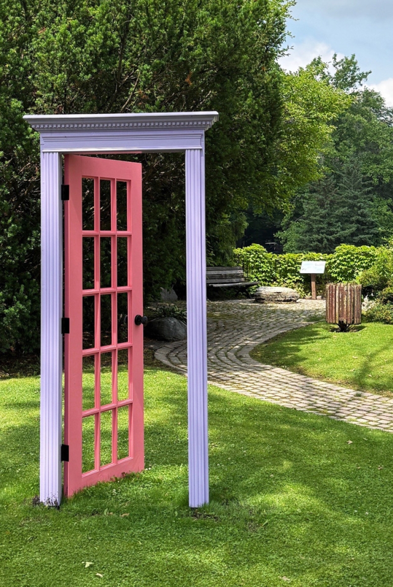 Pink decorative door standing open on a lawn beside a winding garden path.