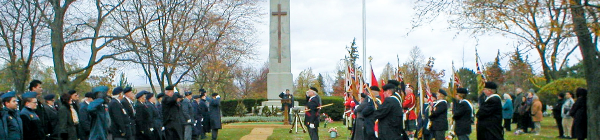 Remembrance Day ceremony at Beechwood with uniformed personnel, flag bearers, and a war memorial under autumn trees.